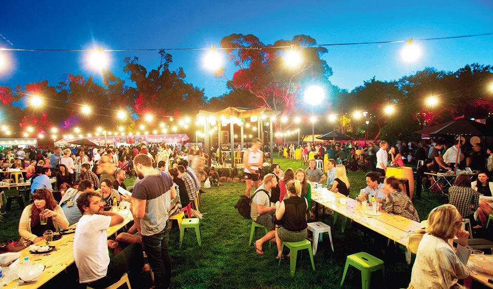 night time scene showing long tables, lights, people eating food as part of a food festival
